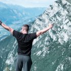 Man standing with arms raised in celebration overlooking a breathtaking mountain landscape.