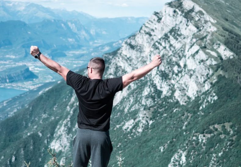 Man standing with arms raised in celebration overlooking a breathtaking mountain landscape.